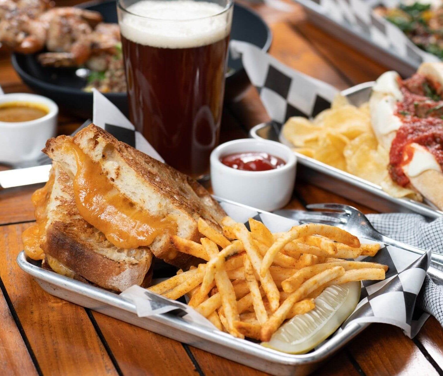 Grilled cheese with fries and a meatball sub next to a cold beer
